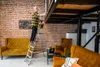 A man is standing on a ladder, working on a loft bed in a living room with brick walls and yellow furniture. Náhľad obrázku produktu