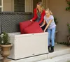 A woman and a girl are putting red cushions into a large, light-colored storage box on a patio. Podgląd zdjęcia produktu