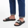 A person wearing blue jeans and black Puma slides. Náhľad obrázku produktu