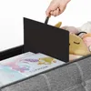 A hand is shown lifting a black divider inside a gray storage bench filled with stuffed animals and books. Náhled obrázku produktu