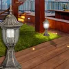 An outdoor patio or rooftop setting with wooden decking, grass, and modern buildings in the background. Two ornate outdoor lamps are illuminated. Náhled obrázku produktu