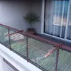 A drying rack is attached to a balcony railing, with a potted plant and a sliding glass door in the background. Voir les images du produit