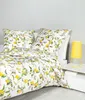 A bed with a lemon-patterned duvet and pillows, next to a bedside table with a yellow lamp. Produktbild-Vorschau