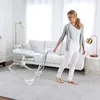 A woman is pulling a baby swing in a living room. Produktbild-Vorschau