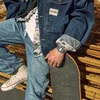 A person wearing a denim jacket and jeans, holding a skateboard. Podgląd zdjęcia produktu