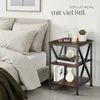 A bedside table next to a bed with pillows and a blanket. Produktbild-Vorschau