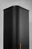 A close-up, studio shot of a tall, black cabinet with a fluted design and a single brass handle. Produktbild-Vorschau