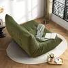 A green sofa is placed on a rug in a living room with sunlight streaming through blinds. Produktbild-Vorschau