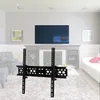 A TV wall mount is shown in a living room setting with a TV mounted on the wall above a fireplace. Náhled obrázku produktu
