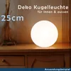 A white spherical lamp is placed on a wooden surface, with decorative straw-like elements to the left. Produktbild-Vorschau