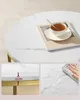 Collage of images showing a white marble coffee table with gold legs. One image shows a cup of tea on the table, another shows a measurement of the table height (15 cm), and the third shows a hand wiping water off the table. Náhled obrázku produktu