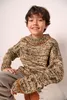 A young boy wearing a knitted sweater and pants sits against a white background. Produktbild-Vorschau