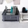 A gray dish drying rack filled with dishes, glasses, and cutlery next to a kitchen sink. Produktbild-Vorschau