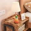 A bedside table with a lamp, a stacking toy, and a framed picture. Podgląd zdjęcia produktu