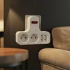 A white power strip with a red on/off switch is mounted on a dark gray wall next to a beige sofa and a wooden table. Produktbild-Vorschau