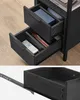 A close-up of two open drawers of a black wooden nightstand. A remote control and books are visible in the drawers. The bottom part of the image shows a single drawer with its slider mechanism. Náhled obrázku produktu