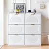 A white shoe cabinet with six flip-down doors is shown in a room with white paneled walls and a light wood floor. Decorative items are placed on top of the cabinet. Anteprima dell’immagine prodotto