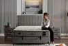 A woman sits on the edge of a bed in a bedroom setting. Produktbild-Vorschau