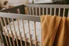 A close-up view of a crib with a blanket draped over the side. Náhled obrázku produktu