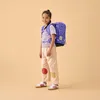 A young girl wearing a backpack stands against a plain background. Náhľad obrázku produktu