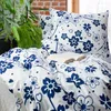 A bed with blue and white floral patterned bedding, pillows, and an open book. Produktbild-Vorschau