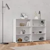 Two white bookshelves are placed against a textured concrete wall, with a floor lamp on the left and a table lamp on the right. The shelves are decorated with various items. Produktbild-Vorschau