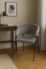 A gray velvet chair is placed next to a wooden desk with a lamp and books. Produktbild-Vorschau