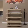 A modern shoe cabinet with four flip-down doors, displaying a light wood finish. The cabinet is placed in a hallway or entryway, next to an umbrella stand. A decorative bowl and vase are on top of the cabinet. Podgląd zdjęcia produktu