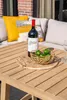 A bottle of red wine and a bowl of limes are placed on a wooden table, with cushions and a brick wall in the background. Produktbild-Vorschau