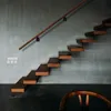 A modern staircase with wooden steps and a wooden handrail against a textured gray wall. A wooden chair is partially visible in the foreground. Náhľad obrázku produktu