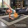 A woman is doing a side plank exercise on a yoga mat in a living room. Produktbild-Vorschau