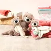 Three plush otter toys are arranged on a wooden floor with blankets and a basket in the background. Náhľad obrázku produktu