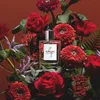 A perfume bottle is surrounded by a bouquet of red flowers and greenery. Náhľad obrázku produktu