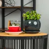 A red cup and saucer sit on a wooden table next to a potted plant. Anteprima dell’immagine prodotto