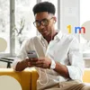 A man is sitting on a yellow couch, looking at his phone while wearing earbuds. Produktbild-Vorschau