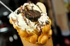 A close-up of a bubble waffle dessert with whipped cream, chocolate drizzle, and cookies. Podgląd zdjęcia produktu