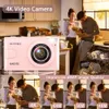 A pink digital camera is shown in the foreground, with a couple in a kitchen in the background. Below the camera are smaller images of the couple, highlighting different resolutions. Produktbild-Vorschau