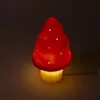 A red mushroom-shaped lamp with white polka dots, lit from within, against a dark background. Produktbild-Vorschau