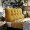 A bedroom scene with a yellow tufted headboard pillow on a bed, next to a nightstand and a lamp. Náhled obrázku produktu