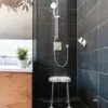 A shower stool is shown in a modern bathroom with black tiled walls. Water is running from the shower head. Produktbild-Vorschau