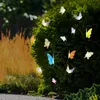 A string of solar-powered butterfly lights is displayed on a green bush, with a blurred background of tall grass and foliage. Produktbild-Vorschau