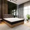 A bedroom scene featuring a large bed with a tufted headboard, a large window with a view of greenery, and a chair. Produktbild-Vorschau