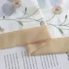 A close-up view of a sheer curtain with embroidered flowers and a beige border, laid over a book. Produktbild-Vorschau