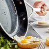 A chef is pouring fried eggs from a pan onto a dish with a piece of toast and greens. Produktbild-Vorschau