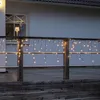 Icicle lights are strung along a wooden railing on a deck at dusk. Podgląd zdjęcia produktu