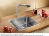 A stainless steel kitchen sink with a modern faucet, set on a wooden countertop with pomegranates and a carafe of red liquid. Produktbild-Vorschau