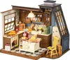 A miniature dollhouse kitchen scene with various accessories and furniture, including a stove, refrigerator, island, and cabinets. Náhľad obrázku produktu