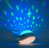 A whale-shaped night light projects stars and dots onto a blue ceiling. Produktbild-Vorschau