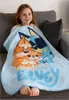 A young girl is sitting on a couch, wrapped in a light blue blanket featuring cartoon dogs and the word "Bluey". Produktbild-Vorschau