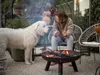 A woman and her dog are sitting by a fire pit in a backyard setting. Voir les images du produit